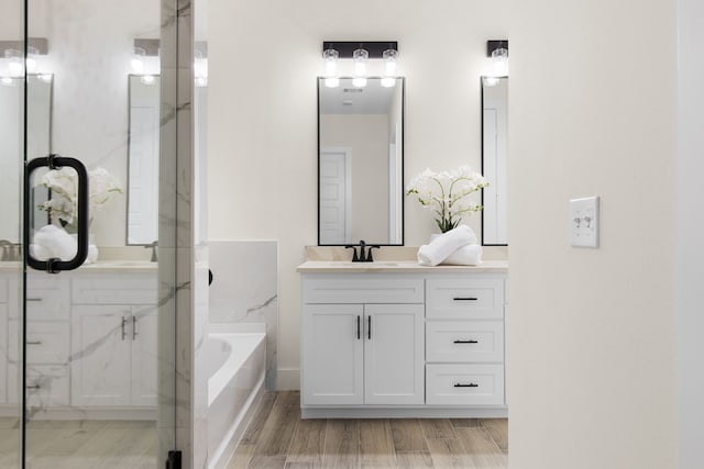 bathroom with a bath, two vanities, a sink, and wood finished floors