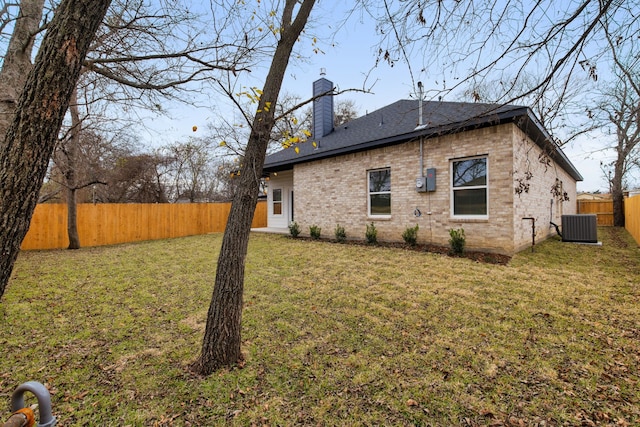 view of property exterior with a fenced backyard, central air condition unit, brick siding, a yard, and a chimney