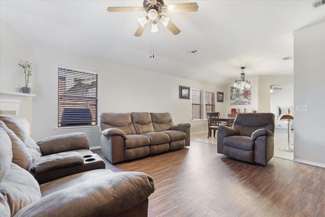 living room with ceiling fan with notable chandelier, visible vents, baseboards, and wood finished floors