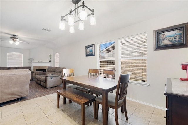 dining area featuring a fireplace, light tile patterned floors, visible vents, baseboards, and ceiling fan with notable chandelier