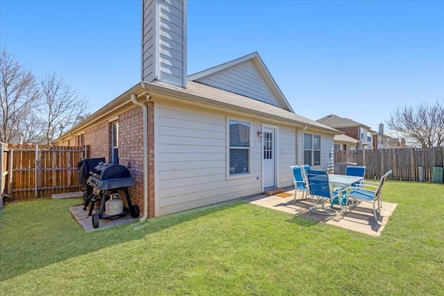 rear view of property featuring a yard, brick siding, a chimney, and a fenced backyard