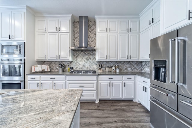 kitchen featuring dark wood finished floors, stainless steel appliances, tasteful backsplash, white cabinetry, and wall chimney exhaust hood