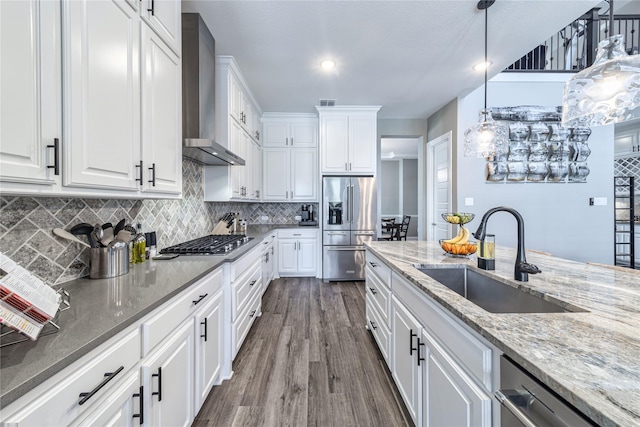 kitchen featuring wall chimney range hood, appliances with stainless steel finishes, a sink, and white cabinetry