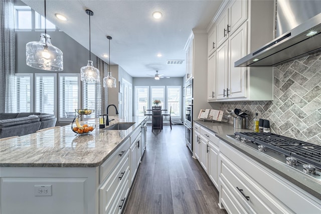 kitchen featuring dark wood-style flooring, visible vents, appliances with stainless steel finishes, a sink, and wall chimney exhaust hood