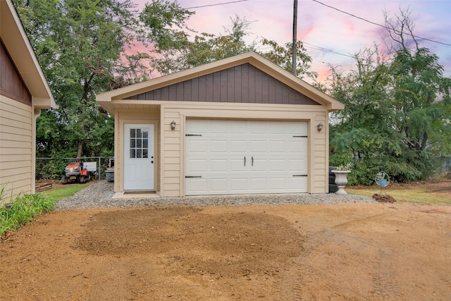 garage at dusk with a detached garage and fence