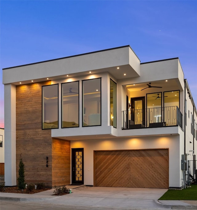 contemporary house featuring driveway, a ceiling fan, a balcony, an attached garage, and stucco siding