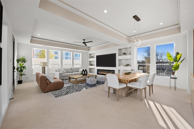 living room featuring built in shelves, a raised ceiling, a glass covered fireplace, and recessed lighting