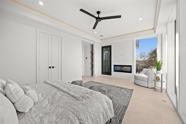 bedroom featuring recessed lighting, light tile patterned flooring, a raised ceiling, and a glass covered fireplace