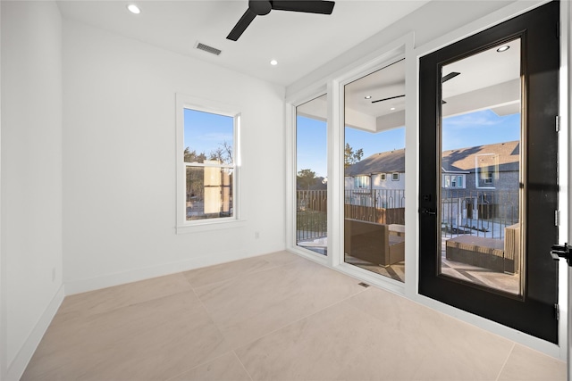 tiled empty room with a healthy amount of sunlight, ceiling fan, visible vents, and baseboards