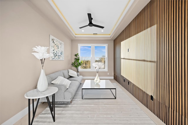 living room with light wood finished floors, a tray ceiling, a ceiling fan, and baseboards