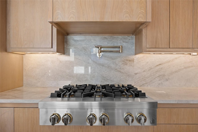 interior details with light stone counters, light brown cabinets, stainless steel gas cooktop, and decorative backsplash