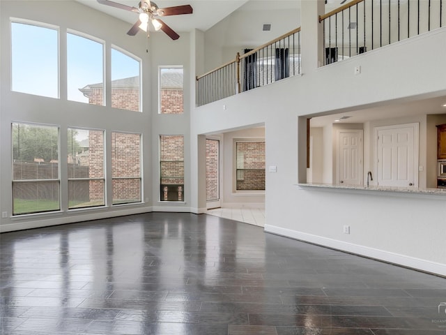 unfurnished living room with a sink, wood finished floors, a ceiling fan, and baseboards