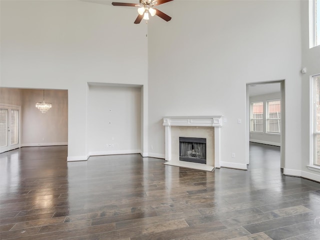 unfurnished living room featuring ceiling fan with notable chandelier, a fireplace, wood finished floors, a towering ceiling, and baseboards