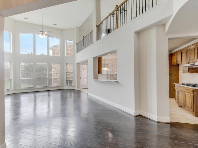 unfurnished living room with a ceiling fan, a towering ceiling, light wood-style flooring, and baseboards