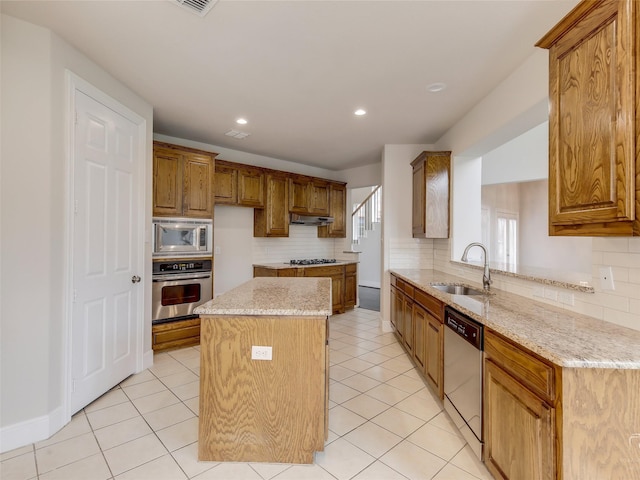 kitchen with light stone counters, under cabinet range hood, stainless steel appliances, a sink, and a center island