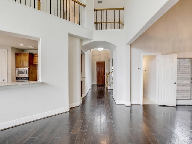 entryway with arched walkways, dark wood finished floors, a high ceiling, baseboards, and stairs