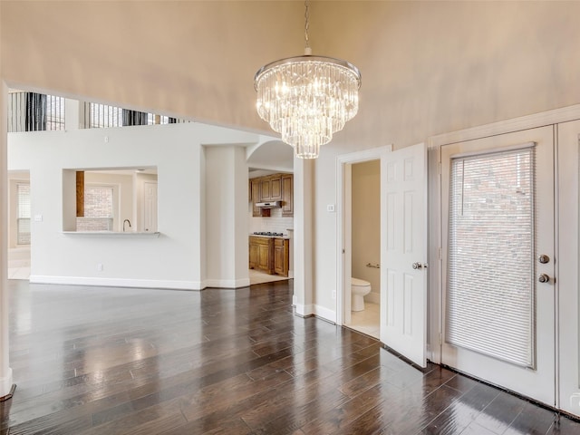 interior space featuring dark wood-style floors, arched walkways, a high ceiling, a chandelier, and baseboards