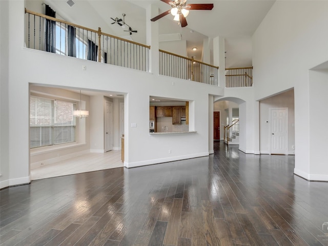 unfurnished living room featuring a ceiling fan, arched walkways, baseboards, and wood finished floors