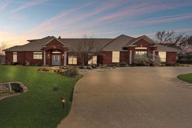 view of front of home with brick siding, a yard, and curved driveway