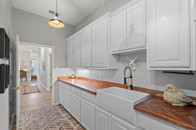 kitchen with visible vents, butcher block countertops, a sink, and white cabinetry