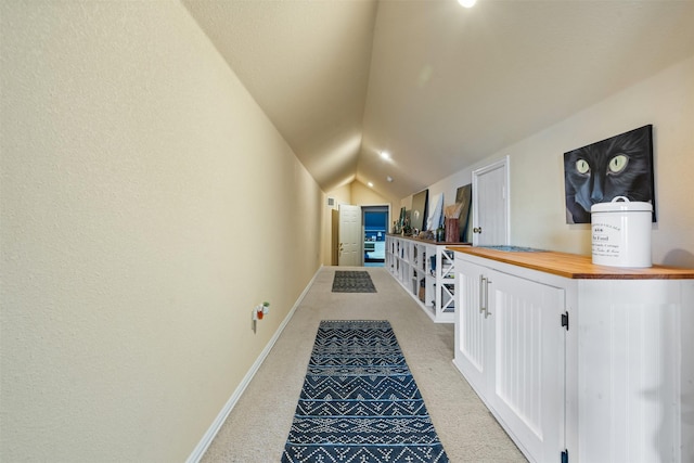corridor with baseboards, vaulted ceiling, and light colored carpet