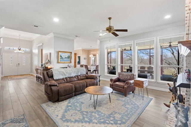 living area with crown molding, ceiling fan with notable chandelier, baseboards, wood finished floors, and visible vents