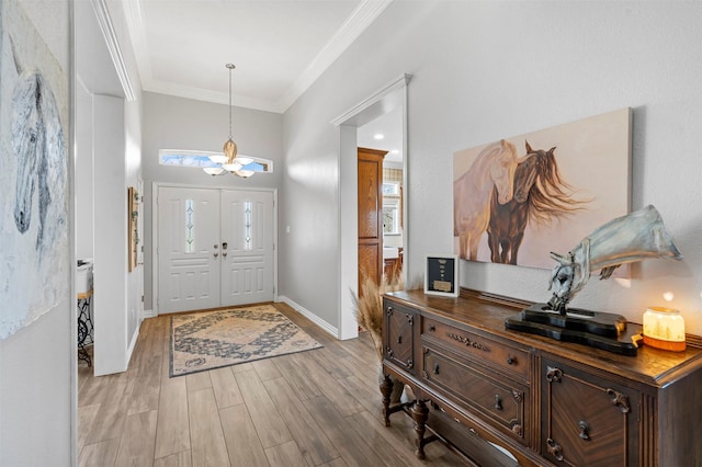entrance foyer with an inviting chandelier, baseboards, ornamental molding, and light wood finished floors