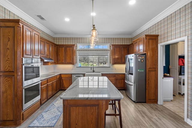 kitchen with appliances with stainless steel finishes, a sink, wallpapered walls, under cabinet range hood, and visible vents