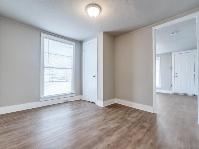 unfurnished room with a textured ceiling, baseboards, and wood finished floors