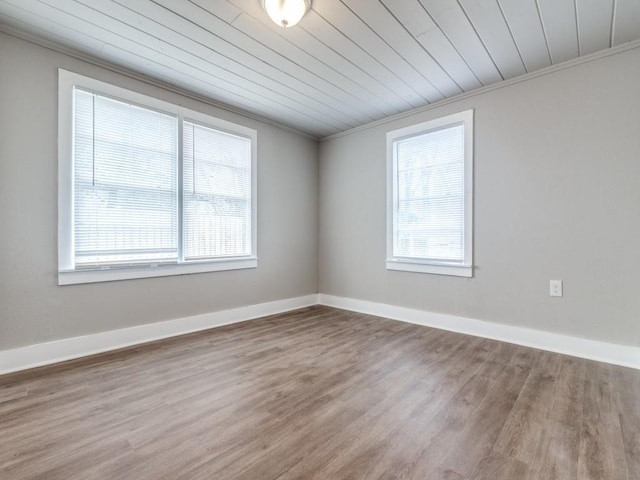 empty room with a wealth of natural light, crown molding, baseboards, and wood finished floors