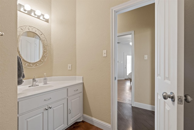 bathroom featuring a textured wall, baseboards, wood finished floors, and vanity