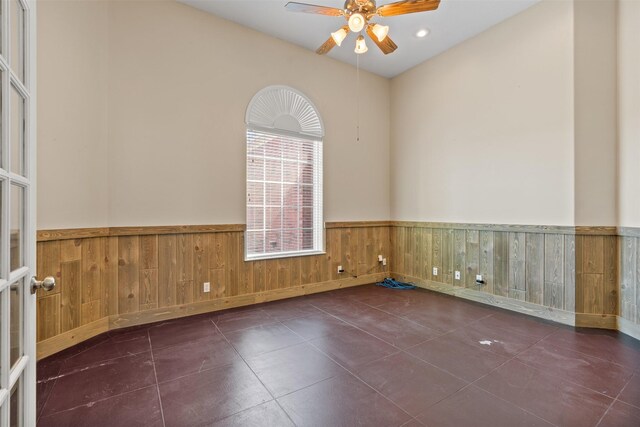 tiled spare room with a wainscoted wall, ceiling fan, and wood walls