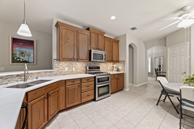 kitchen with arched walkways, visible vents, appliances with stainless steel finishes, brown cabinetry, and a sink