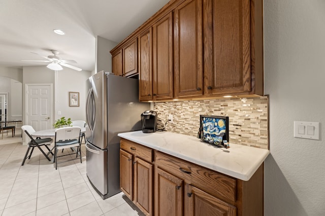 kitchen featuring arched walkways, light tile patterned flooring, freestanding refrigerator, decorative backsplash, and brown cabinetry