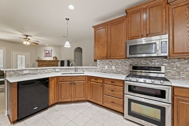 kitchen featuring stainless steel appliances, tasteful backsplash, light countertops, a sink, and a peninsula