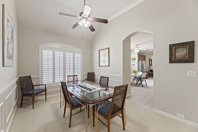 dining area with arched walkways, ceiling fan, a decorative wall, light carpet, and vaulted ceiling