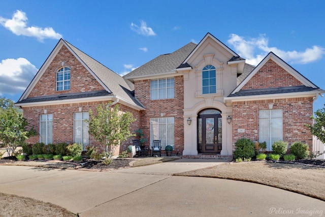 traditional-style house featuring french doors, brick siding, and roof with shingles