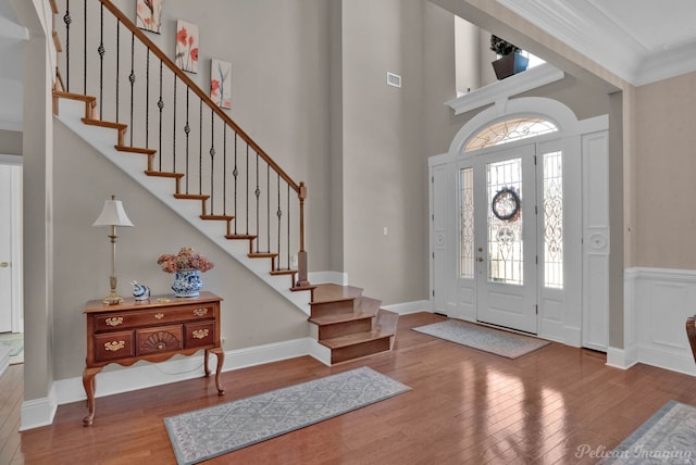 entrance foyer featuring wood finished floors, a towering ceiling, visible vents, stairs, and ornamental molding