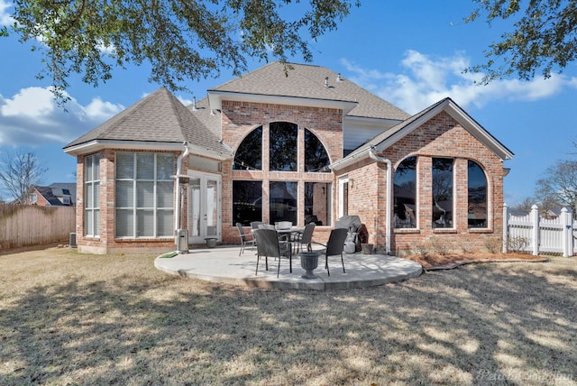 rear view of house with brick siding, a patio area, a fenced backyard, and a shingled roof