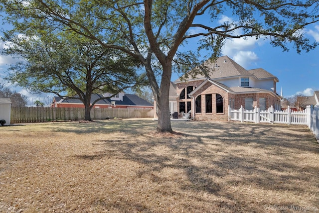 back of house featuring brick siding, a lawn, and fence private yard