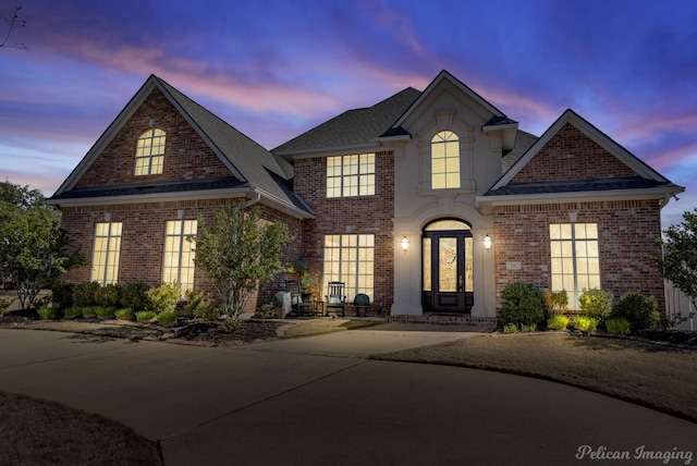 view of front of house with french doors, brick siding, driveway, and roof with shingles