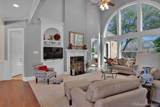 living room featuring built in features, a towering ceiling, ceiling fan, wood finished floors, and a fireplace