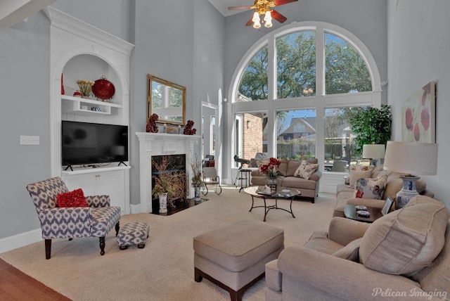 living area featuring baseboards, a ceiling fan, carpet flooring, built in shelves, and a fireplace