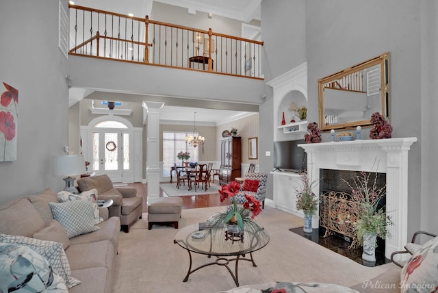 living area with crown molding, a fireplace, a high ceiling, a chandelier, and ornate columns