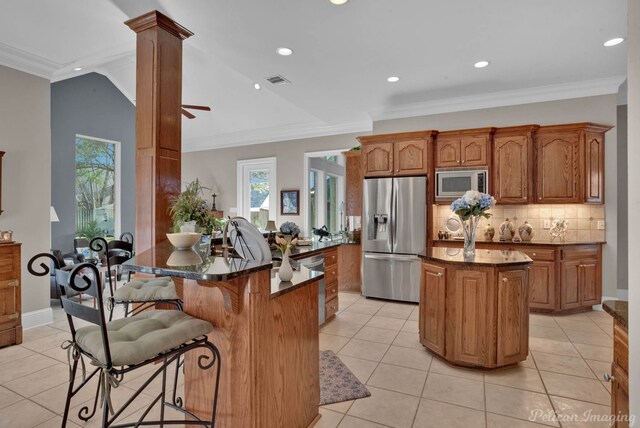 kitchen with appliances with stainless steel finishes, crown molding, decorative columns, and a kitchen island