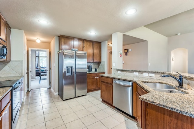 kitchen featuring light stone counters, a sink, appliances with stainless steel finishes, decorative backsplash, and brown cabinetry