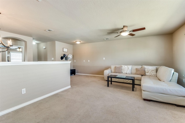 living room featuring arched walkways, light colored carpet, a textured ceiling, baseboards, and ceiling fan with notable chandelier