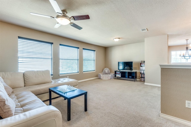 carpeted living area with a textured ceiling, ceiling fan with notable chandelier, visible vents, and baseboards