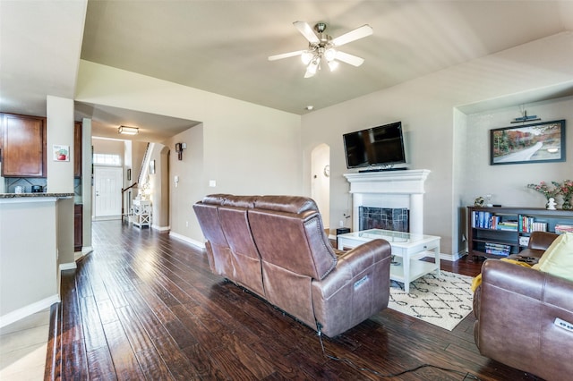 living area featuring baseboards, dark wood finished floors, a ceiling fan, stairs, and a fireplace