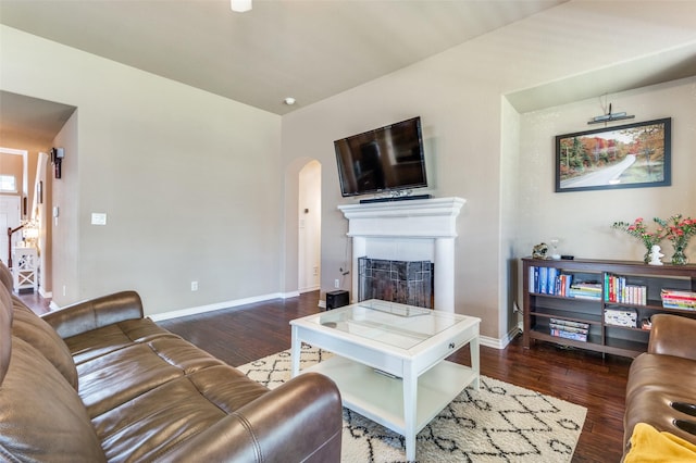 living room featuring arched walkways, a fireplace, wood finished floors, and baseboards